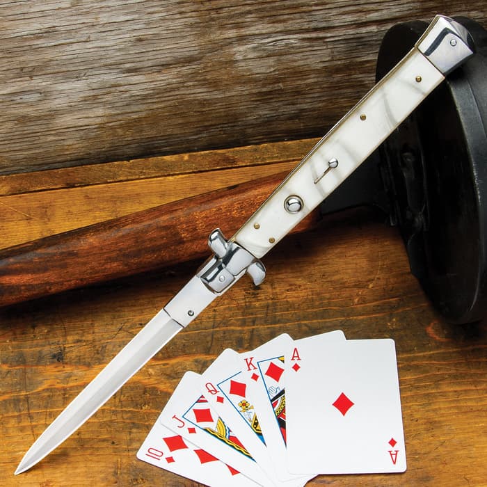 Automatic Italian Pearl Stiletto Knife with stainless steel blade and faux pearl handle scales shown on wooden background with playing cards.