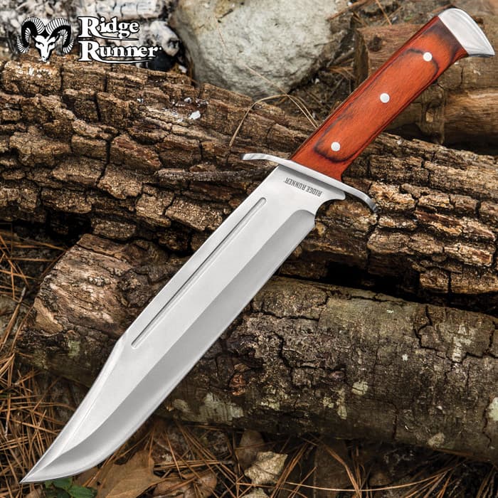 Mirror-polished 9 3/4" bowie knife blade with hand guard and wooden handle on a background of wood, rock, and pine straw. Top left corner "Ridge Runner."

