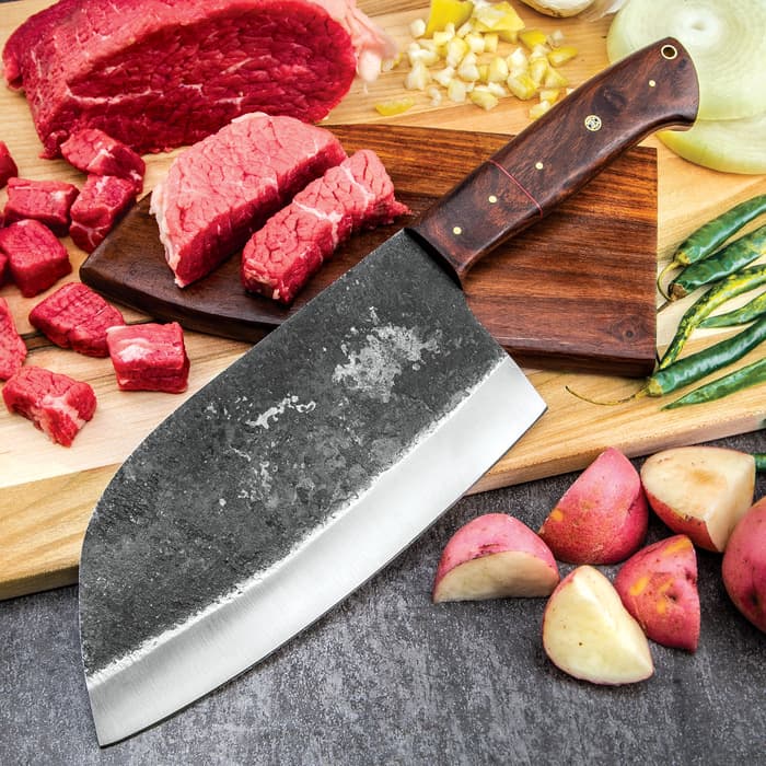 The Timber Wolf Cleaver Butcher Knife with 8” carbon steel blade and wooden handle shown on a chopping board, surrounded by food items.