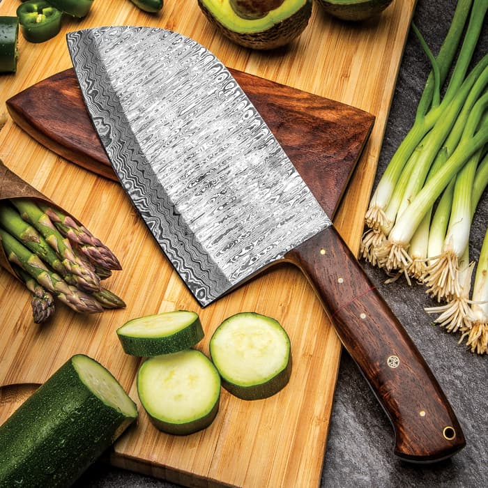 The Timber Wolf Damascus Cleaver Butcher Knife with Damascus steel blade shown on a wooden cutting board, surrounded by vegetables.