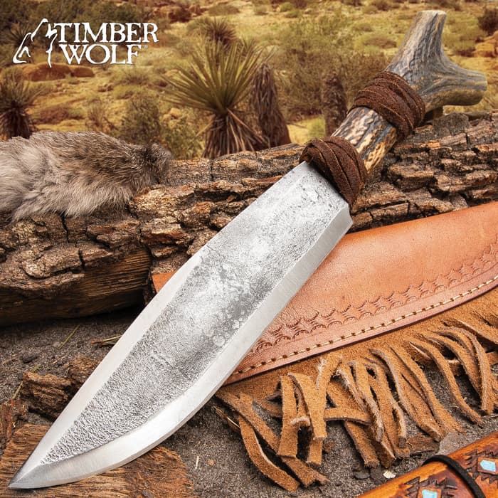 The Timber Wolf Antler Fork Bowie Knife has a rough forged blade and genuine horn handle, shown outside against wood.