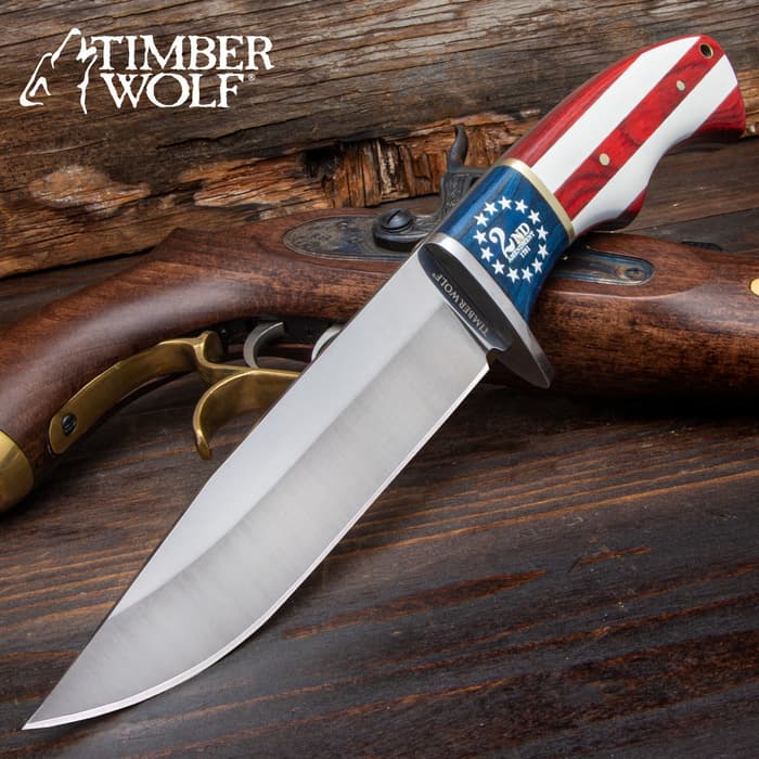 Large bowie knife with a silver blade and American flag handle with “2nd Amendment” printed onto the flag, positioned on an antique wood pistol and wood background.