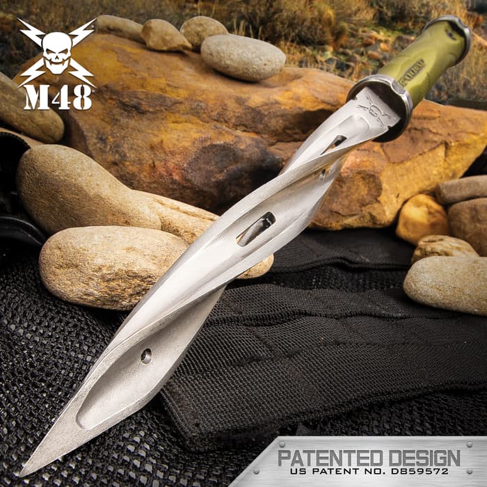 The M48 Battle Scarred Series Olive Drab Cyclone has a 8” cast stainless steel blade with three spiraling cutting edges, shown leaned against rocks.