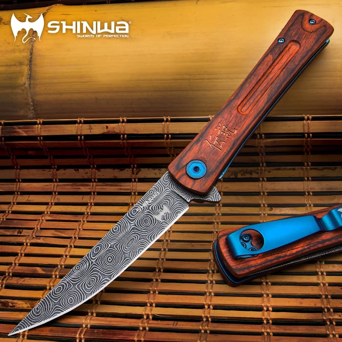Slim open pocket-knife with bloodwood handle, metallic blue accents, and grey upswept blade with a raised raindrop pattern on a background of bamboo.
