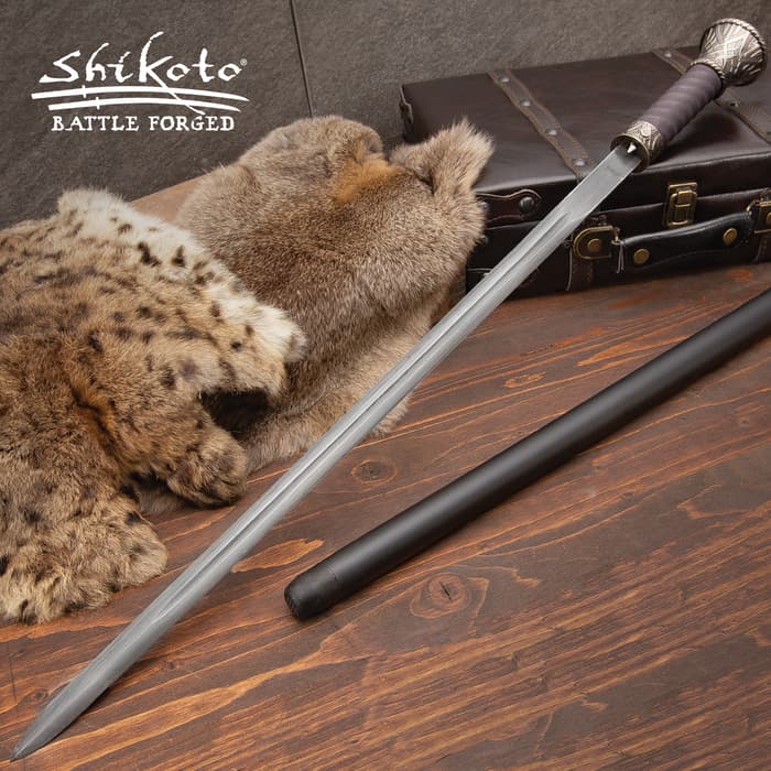 Shikoto sword cane with leather handle and Damascus steel blade shown atop a leather case, next to animal skins. 