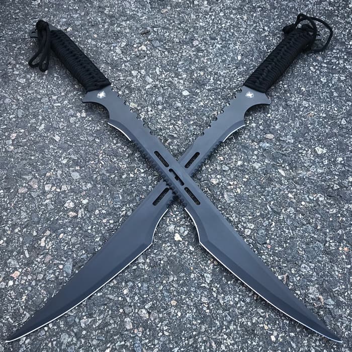 Secret Agent dual swords with black blades and black cord wrapped handles are laid across each other on pavement. 