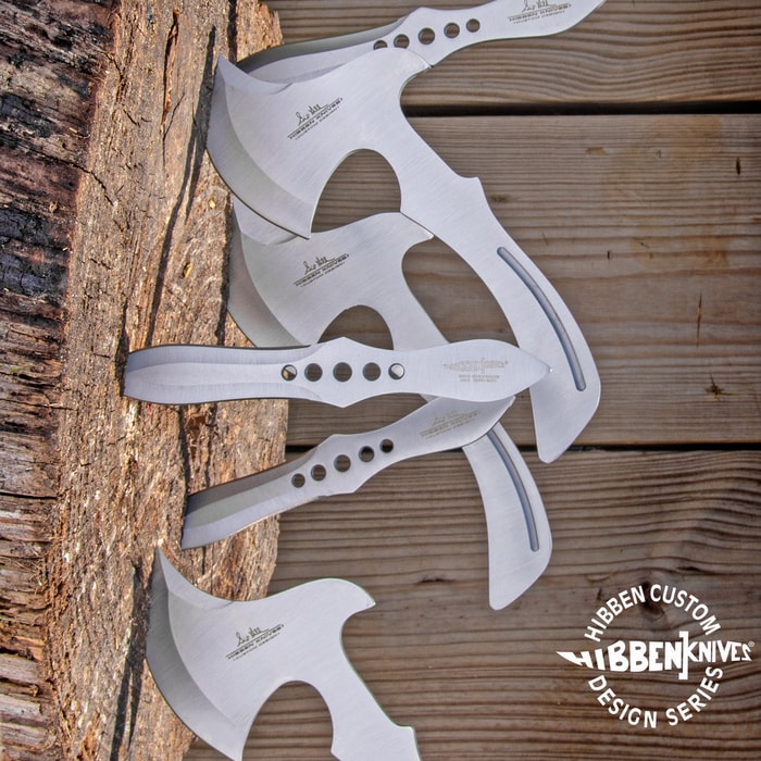 3 stainless steel throwing knives and 3 stainless steel throwing axes imbedded in a wooden stump. Bottom right corner "Hibben Custom Design Series" encircling "Hibben Knives" logo. 

