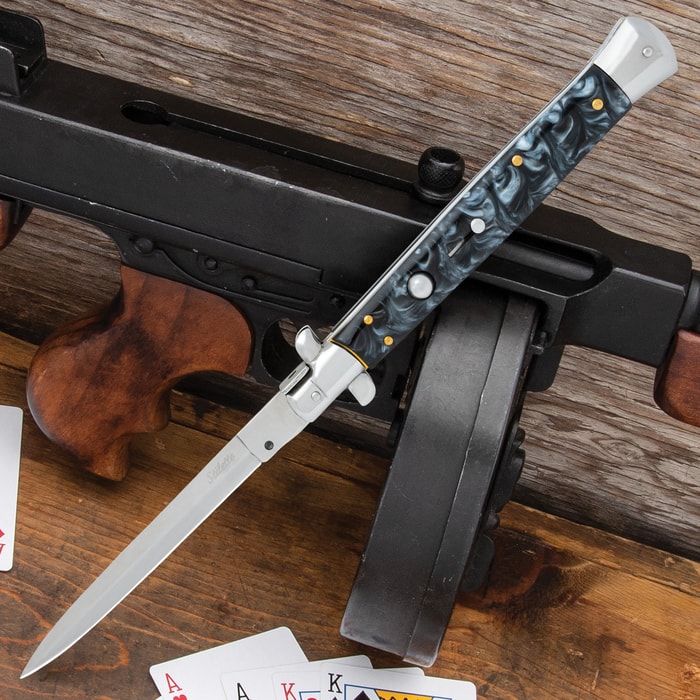 Automatic Italian Black Stiletto Knife with stainless steel blade and black acrylic handle shown laid against a firearm.