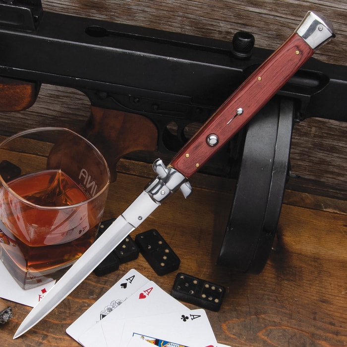 Automatic Italian Wooden Stiletto Knife with stainless steel blade and wooden handle shown laid against a firearm.