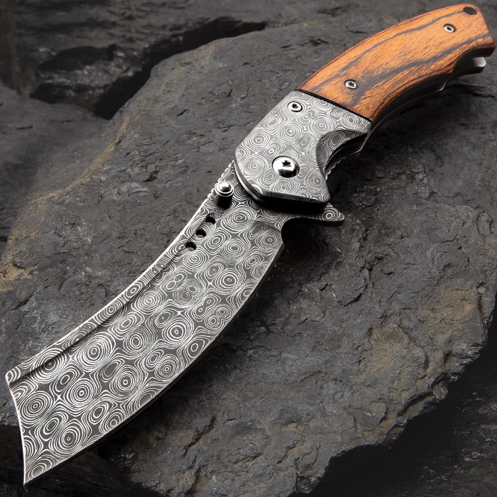 The Boot Hill Razor Pocket Knife is shown with 3 1/2" Damascus patterned stainless steel blade and wooden handle on a dark rock background.