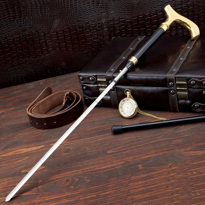 A sword cane with black and gold detailing is shown with belt, pocket watch, and briefcase in the background. 
