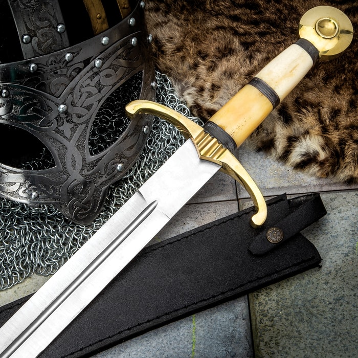 Camelot Sword shown with bone handle and brass-colored guard adjacent to a helmet and animal pelt. 