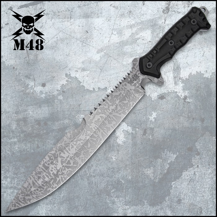 Combat machete with spiderweb titanium electroplated finish and a partial sawback spine on a background of black and tan utility gear.